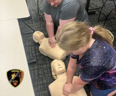 Two people practicing CPR on dummies, Chaska Fire Department logo
