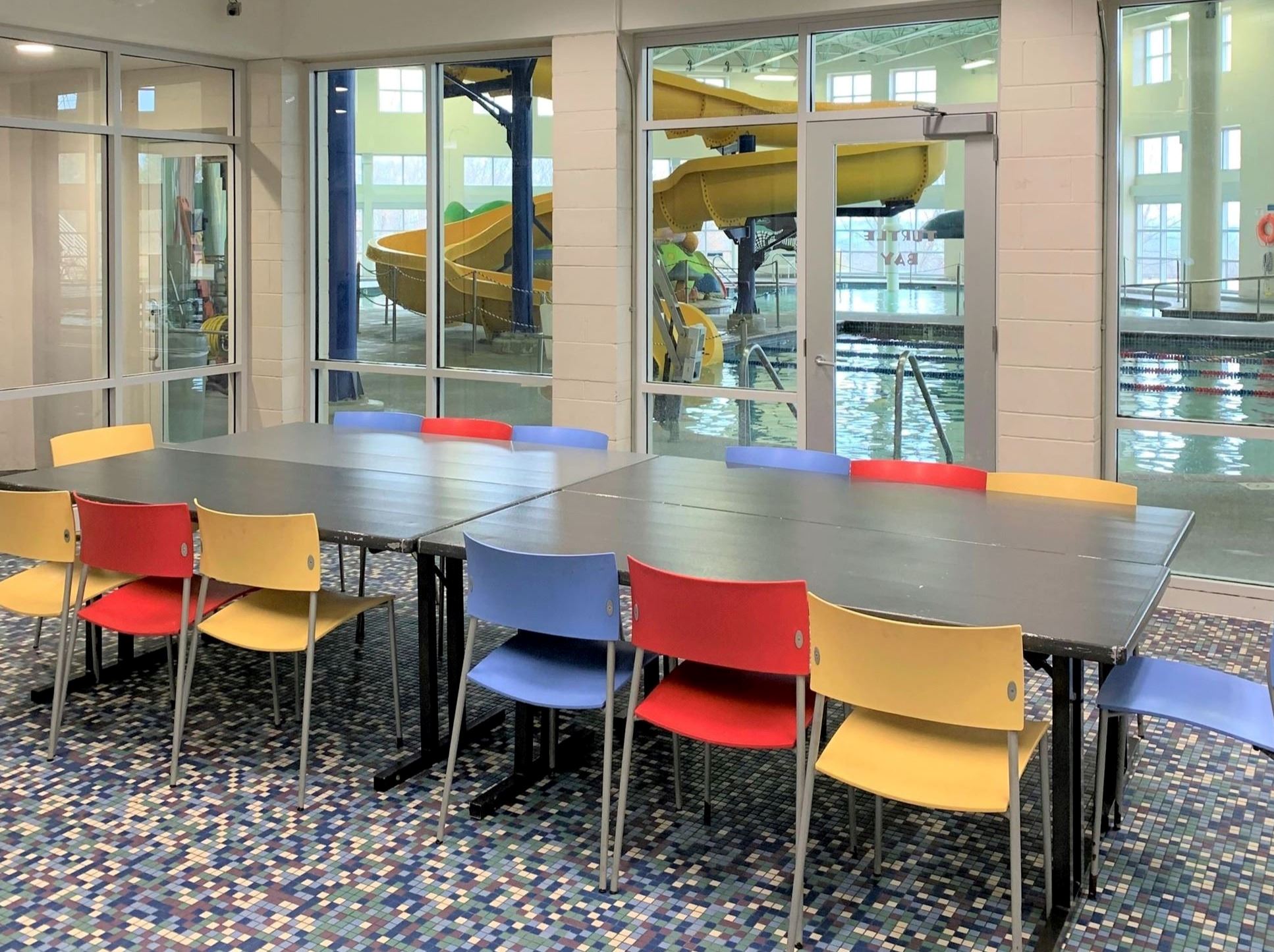 Photo depicts table with 13 colorful chairs, in the back you can see the pool with big yellow slide